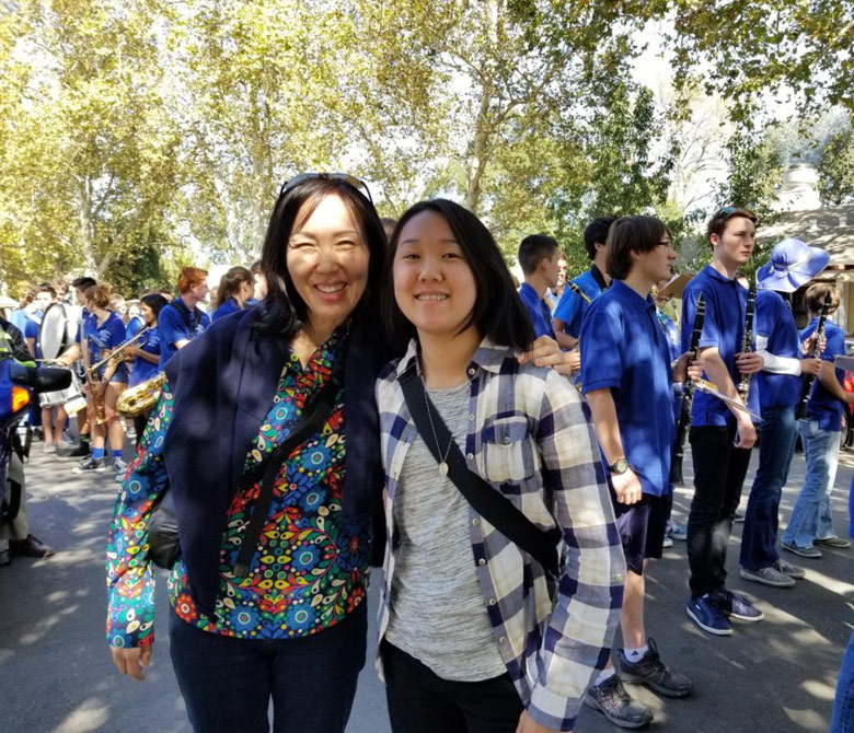an image of two young Asian American women standing together for a photograph with lots of people behind them in the background